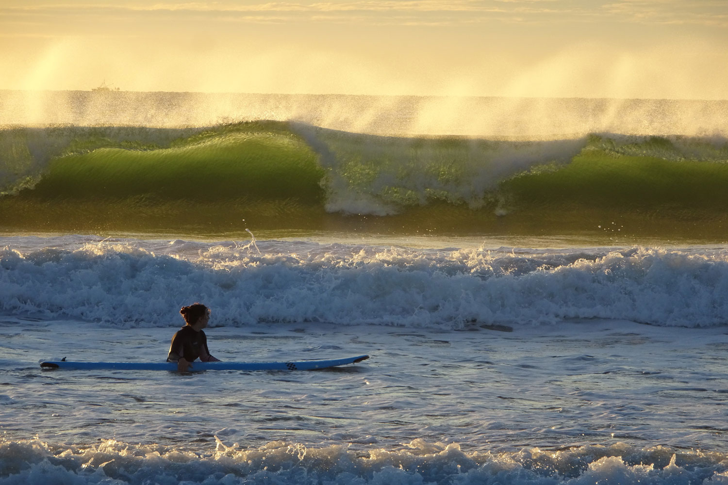 Ein Surfer bei Wellengang im glitzernden Licht der aufgehenden Sonne. 