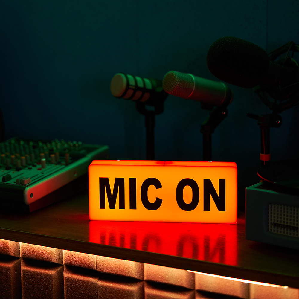 Mikrofon auf einem Tripod, leuchtendes Neonschild das Podcast-Aufnahme signalisiert