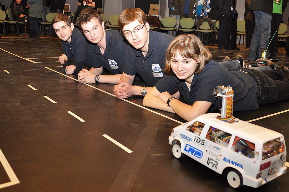 Studierende betrachten ein autonomes Modellfahrzeug beim Carolo Cup