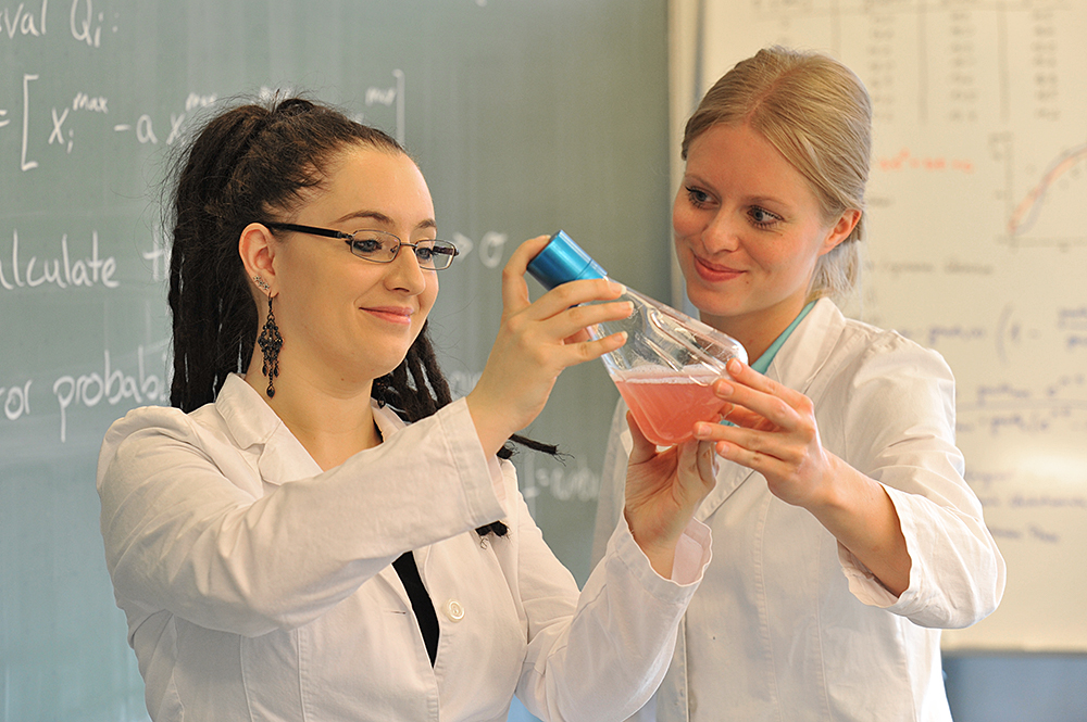 Zwei Studentinnen betrachten einen Erlenmeyerkolben am Institut für Mikrobiologie