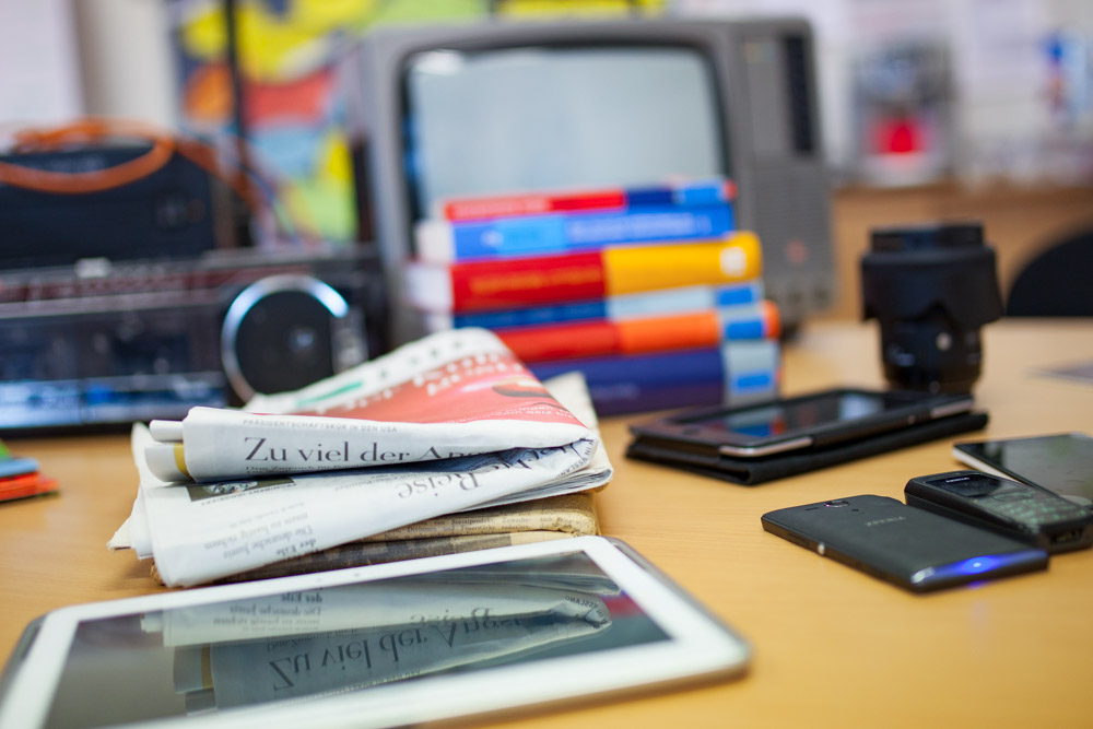 Symbolfoto: Zeitung, Bücher, Kamera, Smartphones und Tablet auf einem Schreibtisch