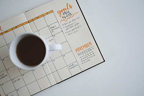 A cup of coffee on a notebook with a calendar