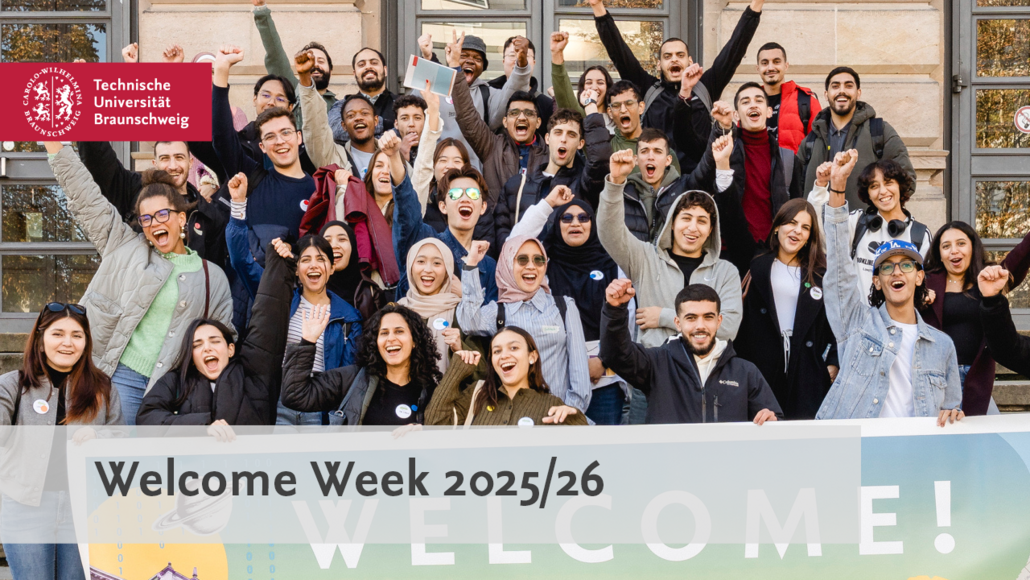 [Translate to English:] A group of students stands behind a large banner with the word ‘Welcome’ written on it and cheers.