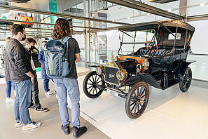 Students are standing in front of a historical old car