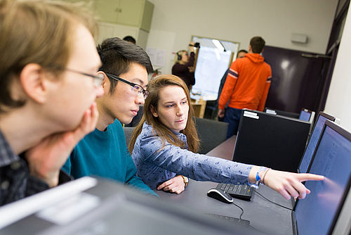 Eine Studierende zeigt ihren Kommilitonen etwas auf einem Monitor