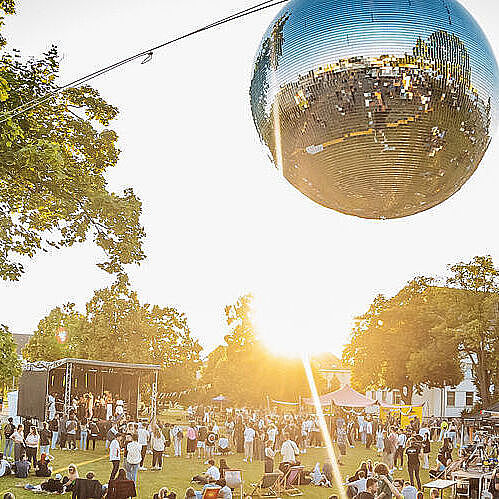 Zu sehen ist ein Bild von einem Festivalgelände inklusive Bühnen, Diskokugel und Personen.