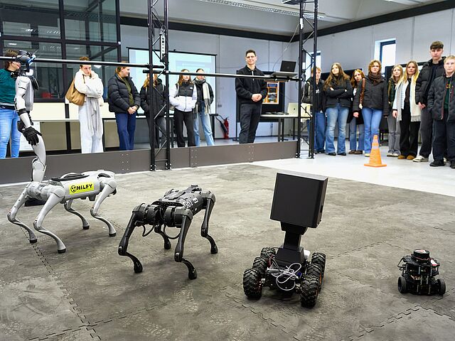 Schülerinnen und Schüler schauen auf aufgereihte Roboter