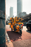 Eine Skyline im Hintergrund. Im Vordergrund steht ein Motoroller, der viele orangefarbene Fahrräder transportiert. 