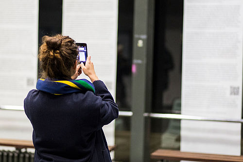 Eine Studierende fotografiert Poster an einer Wand