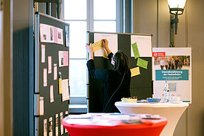 A conference participant writes a card and pins it on a pinboard.