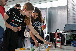 Einige junge Menschen stehen an einem Messestand und schauen interessiert die Ausstellungsstücke an