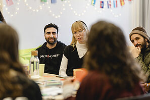 Studierende sitzen an den Tischen in der Welcome Lounge und unterhalten sich miteinander. 