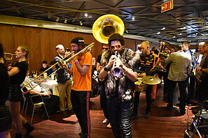 Costumed people play wind and percussion instruments and are observed and filmed with mobile phones.