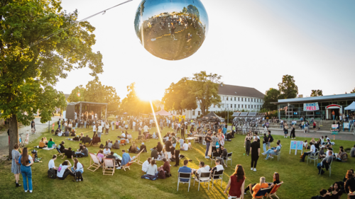 Besucher eines TU-Festivals sitzen auf einer Wiese am Campus Nord