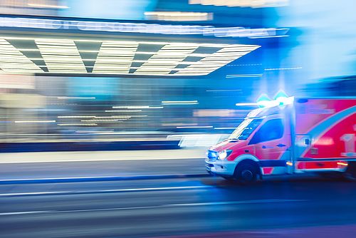 An ambulance is driving with blue lights. The background is very blurred.