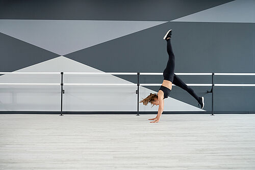 Female dancer practicing wheel jump in dance hall.