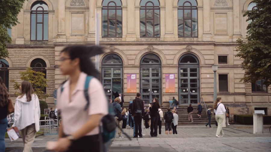 Menschen stehen auf dem Universitätsplatz und im Hintergrund ist das Altgebäude der TU Braunschweig zu erkennen. An der Fassade hängen HIT Plakate