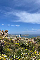 Drei Personen stehen auf einer Anhöhe und schauen auf die griechische Berg- und Meerlandschaft.
