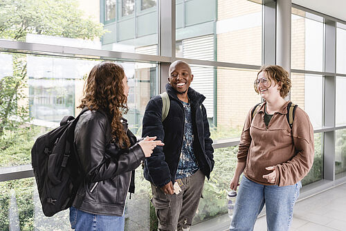 Three students are standing together and talking happily.