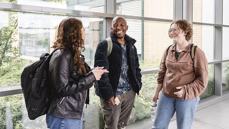 Three students are standing together and talking happily.