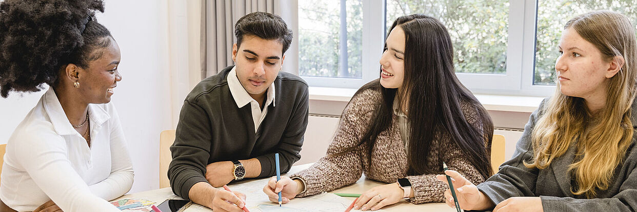 Vier Studierende sitzen an einem Tisch und arbeiten gemeinsam an einem Projekt.  