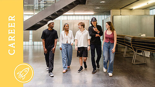 Fünf Studierende gehen nebeneinander auf die Kamera zu und unterhalten sich dabei. 