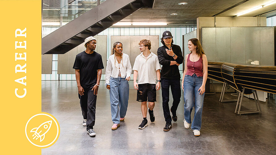 Fünf Studierende gehen nebeneinander auf die Kamera zu und unterhalten sich dabei. 