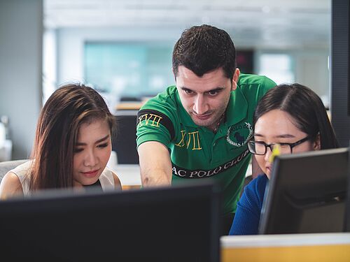 Drei Studierende sitzen vor einem Computer und reden miteinander. 
