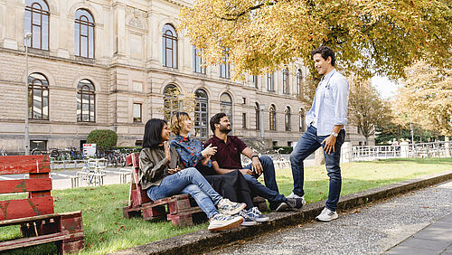 Internationale Studierende sitzen vor dem Altgebäude der TU Braunschweig und unterhalten sich.