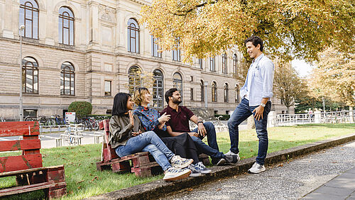 International students sit and chat in front of the Historic Main Building of TU Braunschweig. 