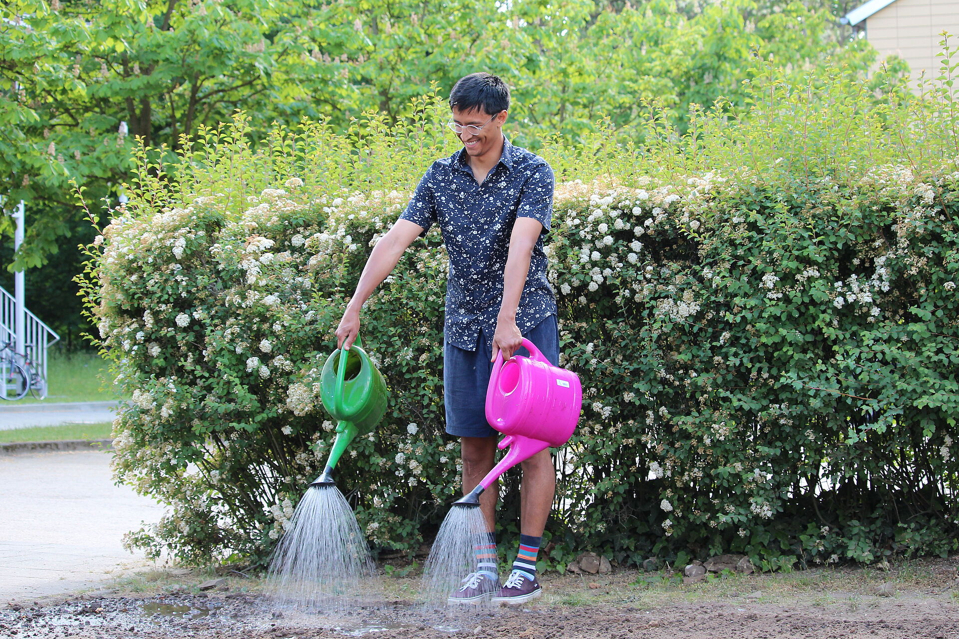 Person mit zwei Gießkannen gießt Wasser auf Erde