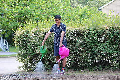Person mit zwei Gießkannen gießt Wasser auf Erde