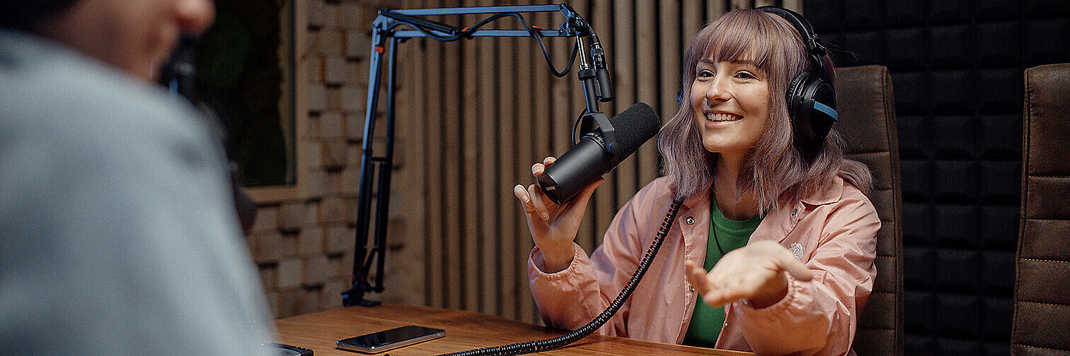 Junge Frau moderiert vor einem Mikrofon Podcast  