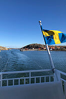 Blick von einer Fähre auf schwedische Inseln. Am Schiff weht eine schwedische Flagge.