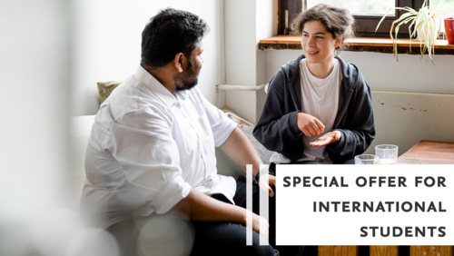 Zwei Studierende unternhalten sich. Auf dem Tisch vor ihnen stehen Tassen mit Kaffee. Auf dem Bild steht die Aufschrift "Special offer for international students". 