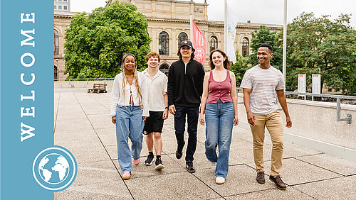 Fünf internationale Studierende gehen fröhlich auf die Kamera zu. Im Hintergrund ist das Altgebäude zu sehen.