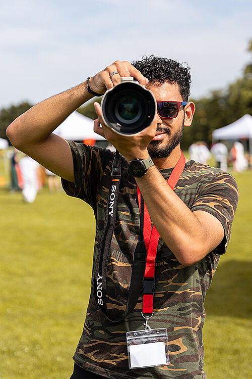 Fotograf Ahmed mit Kamera vor dem Gesicht frontal aufgenommen