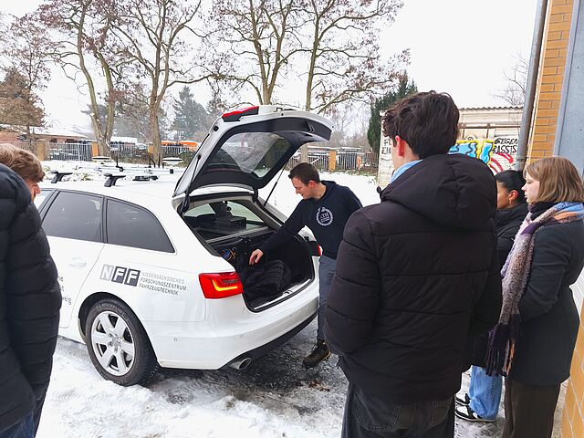 Person zeigt Schülerinnen und Schülern den Kofferraum eines Autos der TU Braunschweig