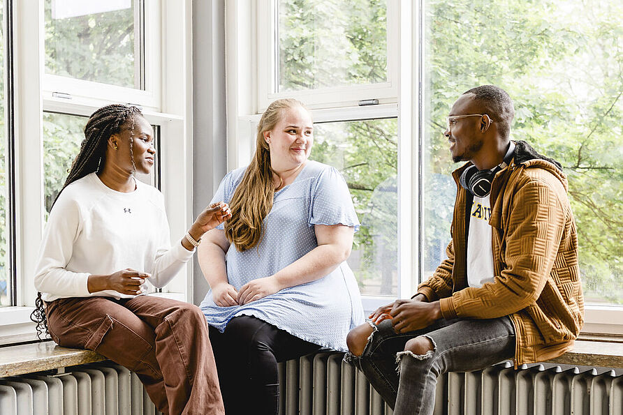 Drei Studierende sitzen im Altgebäude der TU Braunschweig und unterhalten sich miteinander.