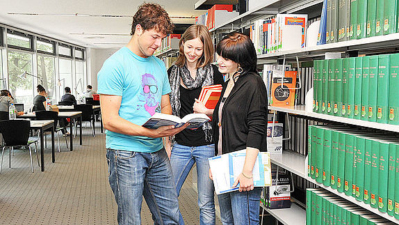 Studierende vor einem Bücherregal in der Bibliothek