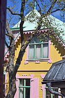 Ein sehr farbenfrohes Haus mit grünem Dach, orangefarbenen Wänden und rosa Fensterdekorationen.