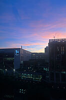 Eine dunkle Stadtskyline mit einem sich rötlich färbenden Himmel im Hintergrund.