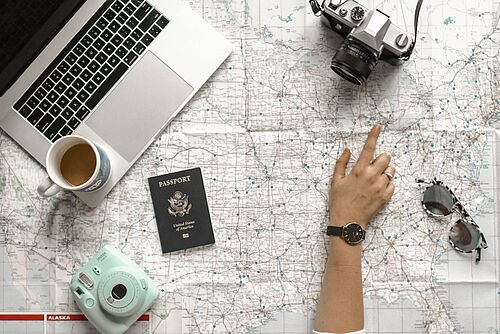 One person is studying a card with a laptop, a coffee cup, two cameras, an American passport and a pair of sunglasses on it.