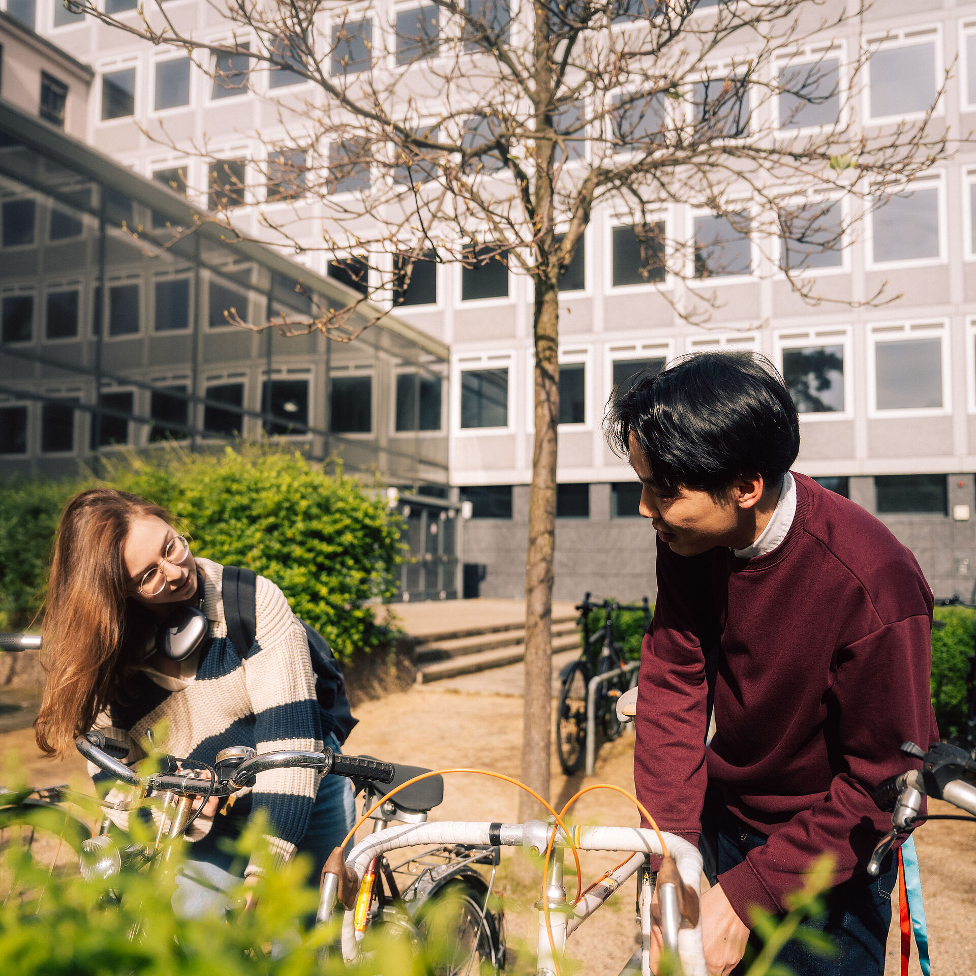 Zwei Studierende der TU Braunschweig sprechen miteinander während sie ihre Fahrräder am Campus abschließen.