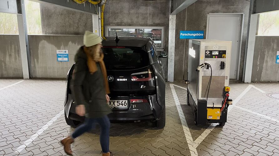 Autofahrerin geht zur mobilen Ladeplattform Nimbee in einem Parkhaus