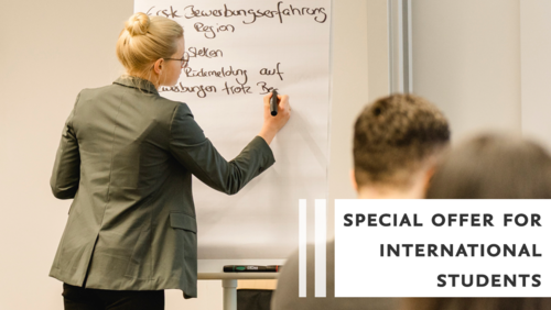 Eine Frau schreibt etwas an ein Whiteboard. Man sieht die Rücken von einzelnen Studierenden im Seminarraum.