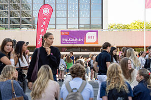 Schülerinnen und Schüler sammeln sich auf dem Universitätsplatz der TU Braunschweig. Die Stimmung ist locker und ausgelassen. Im Hintergrund ist am Audimax ein Banner mit der Aufschrift Willkommen: Dein Tag an der Uni zu sehen