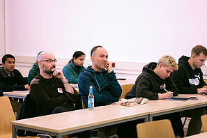 Workshop participants sit in a seminar room and listen intently.