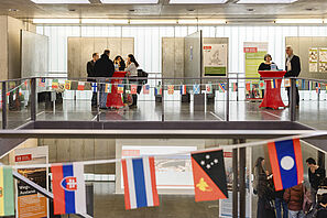 Blick in den mit Fahnen geschmückten Architekturpavilllon. Im Hintergrund findet Beratung an Stehtischen statt.