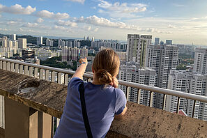 Die Studentin steht uaf einem Wohngebäude in Queenstown und genießt den Ausblick über die Stadt Singapur. 